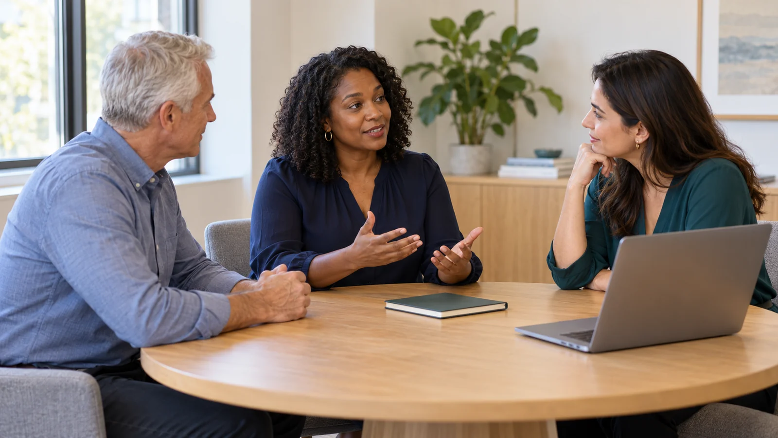 Illustrative scene of three colleagues discussing a work plan around a meeting table.